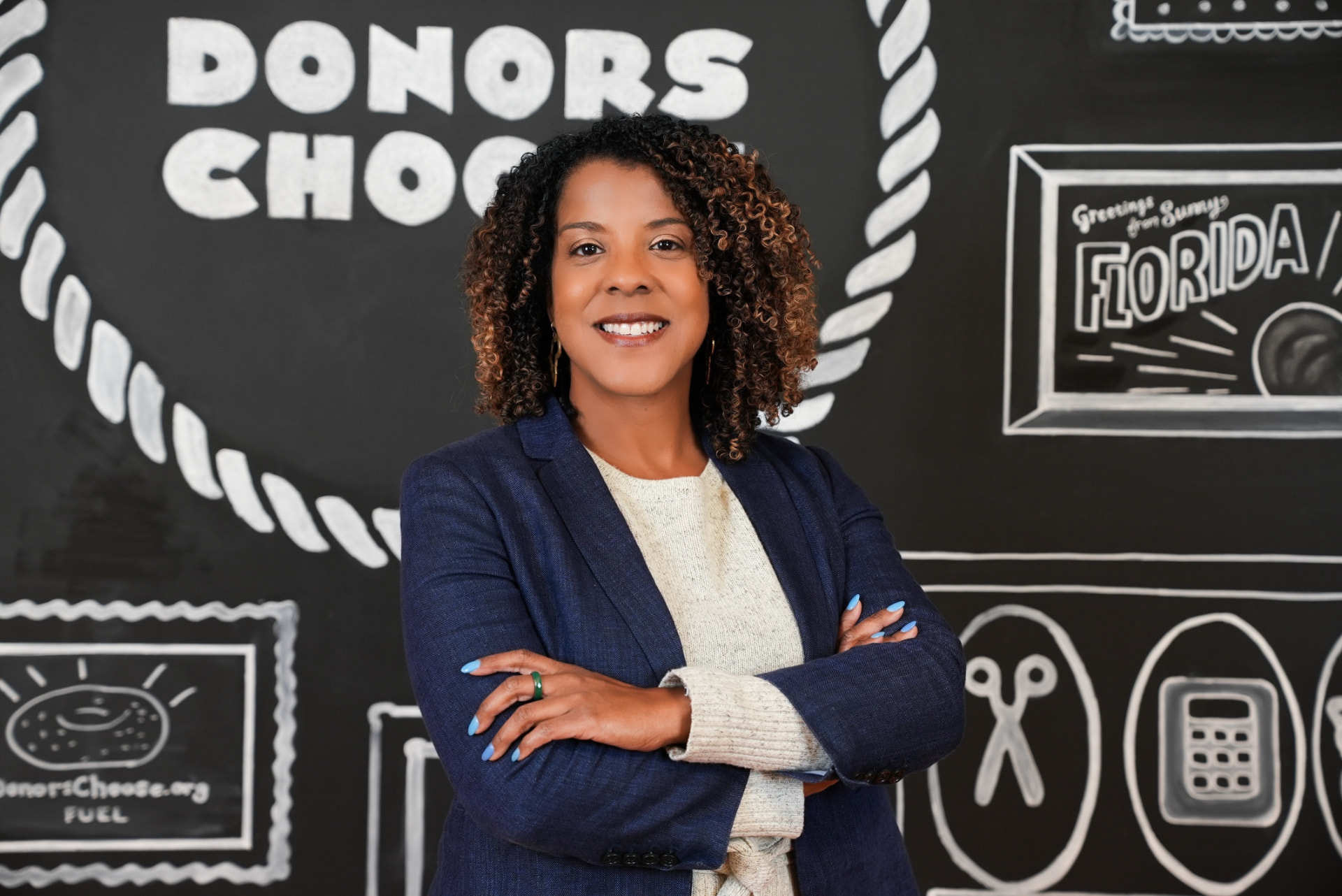 Jinan O'Connor in a navy blazer standing in front of a DonorsChoose chalkboard