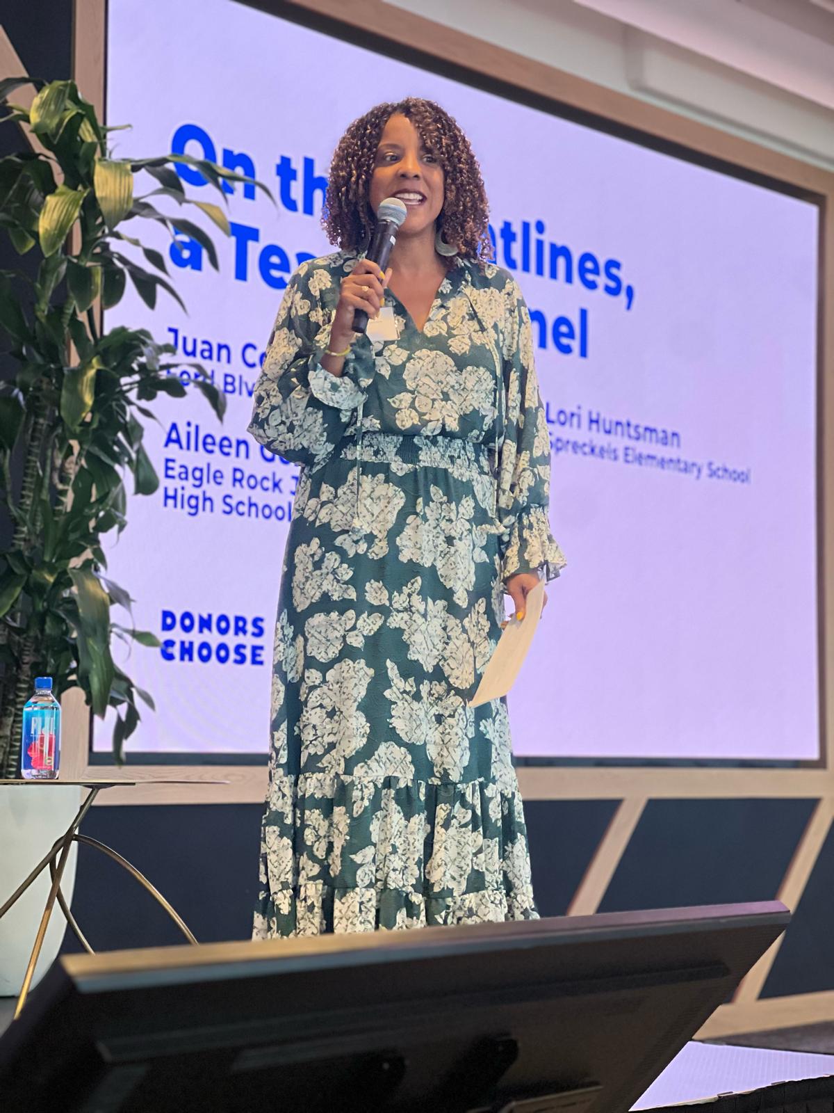 Jinan O'Connor speaking into a microphone on stage during a DonorsChoose teacher panel